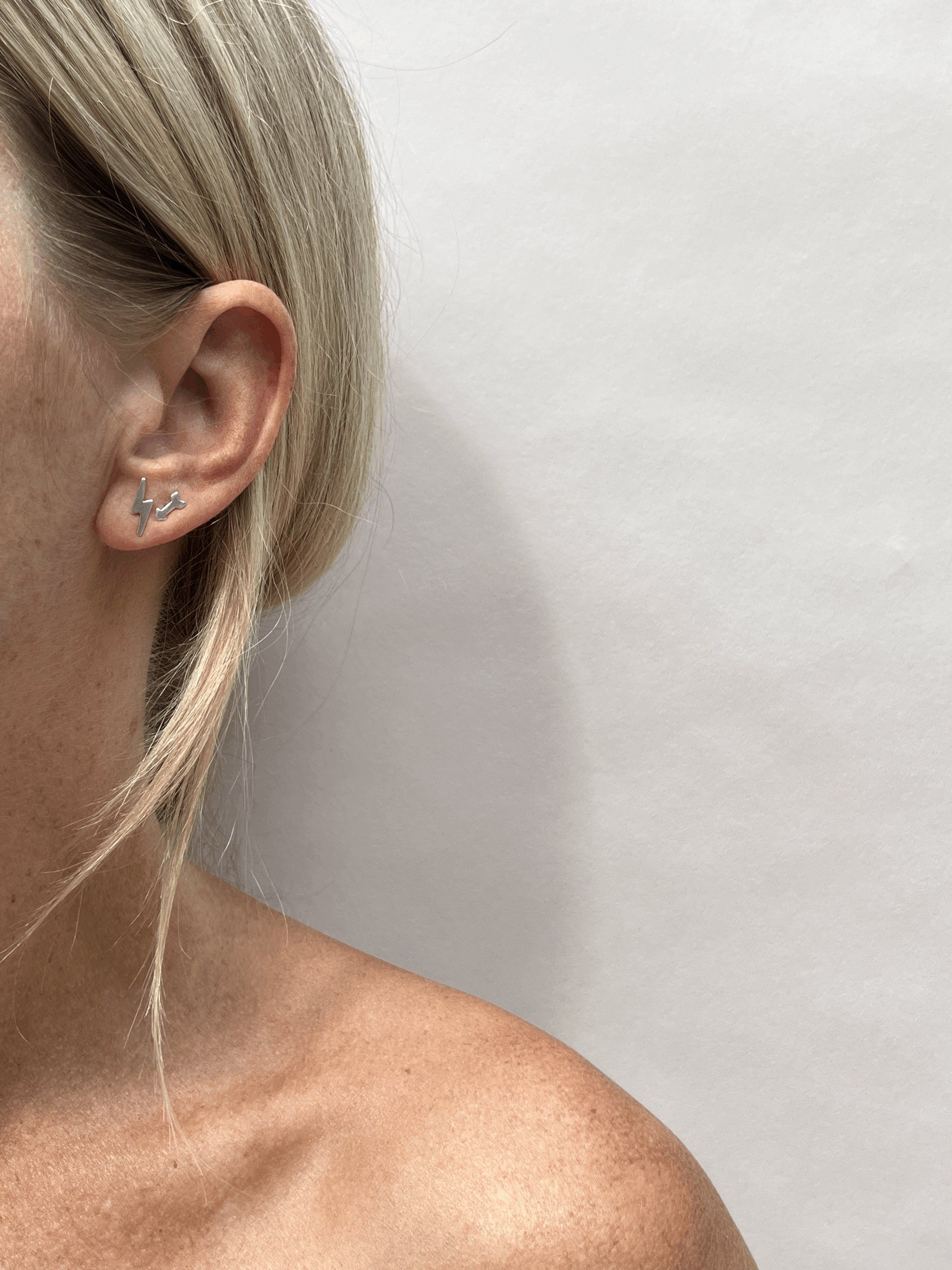 Model wearing a sterling silver lightning bolt stud earring in her first ear piercing and an arrow stud earring in her second ear piercing, different angle