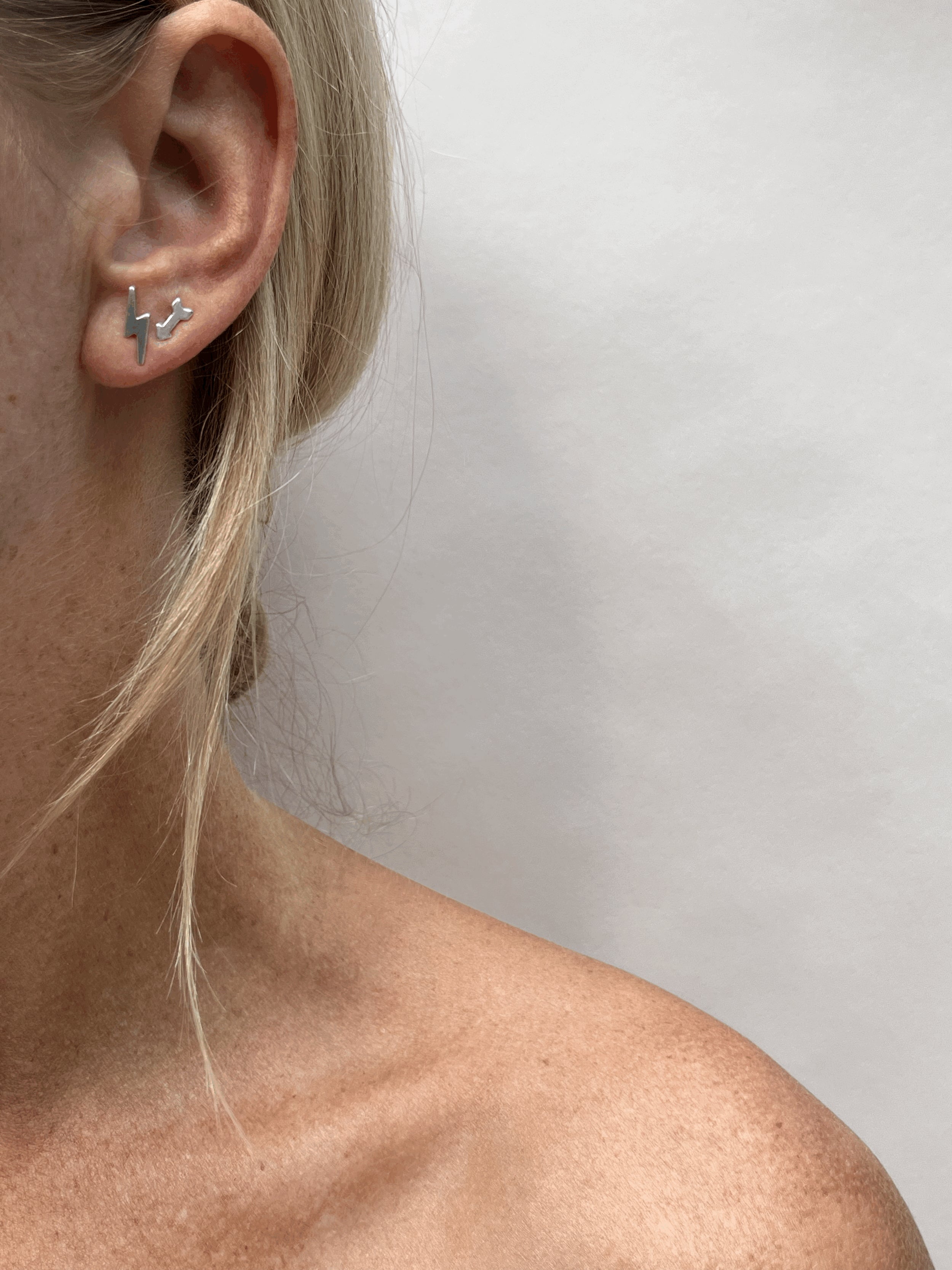 Model wearing a sterling silver lightning bolt stud earring in her first ear piercing and an arrow stud earring in her second ear piercing