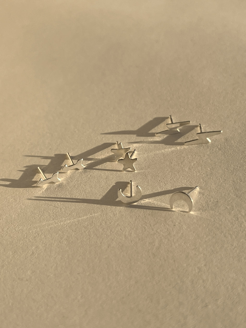 Four pairs of sterling silver stud earrings—lightning bolt, star, arrow, and moon—displayed together on a neutral background