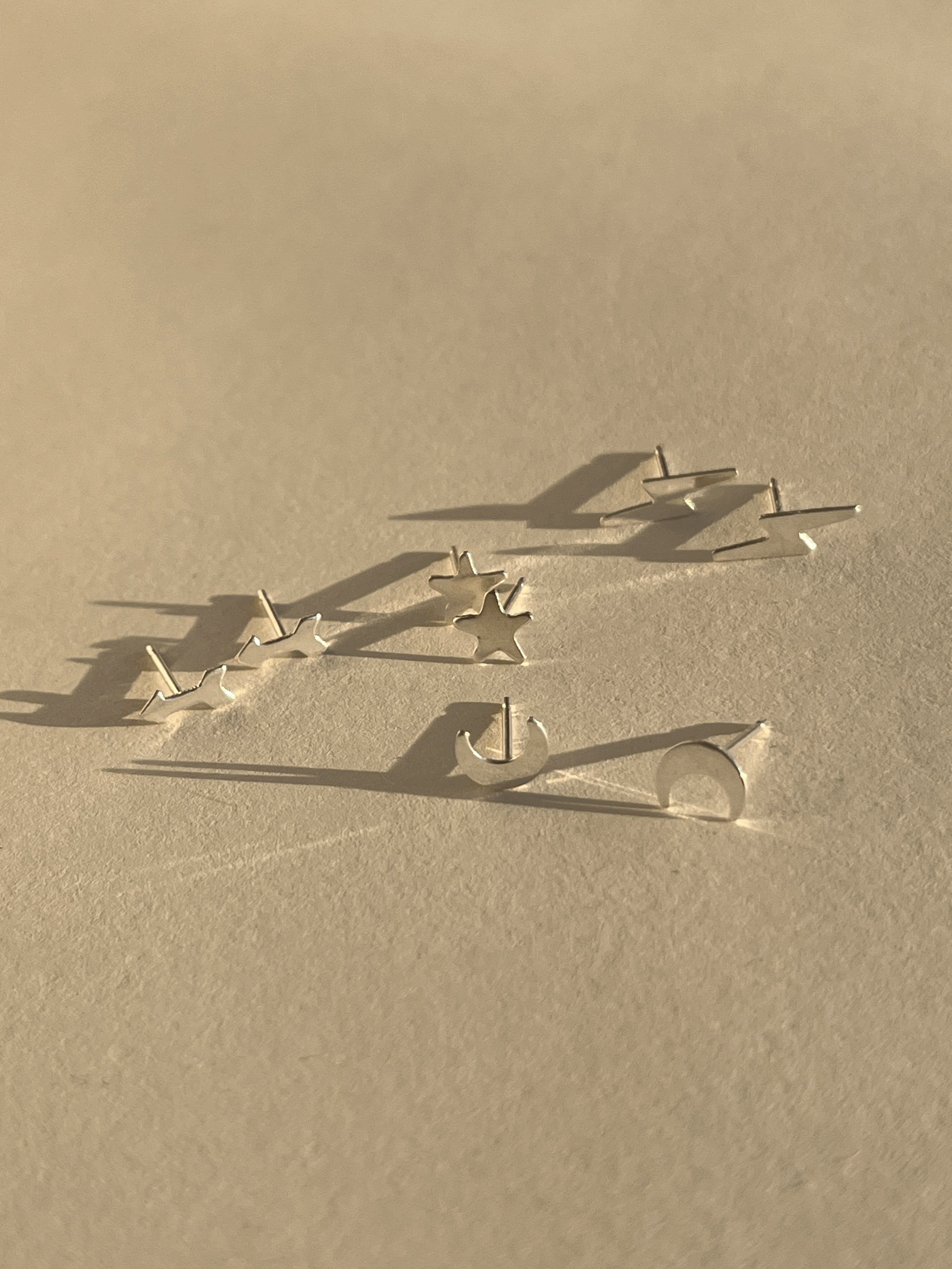 Four pairs of sterling silver stud earrings—lightning bolt, star, arrow, and moon—displayed together on a neutral background