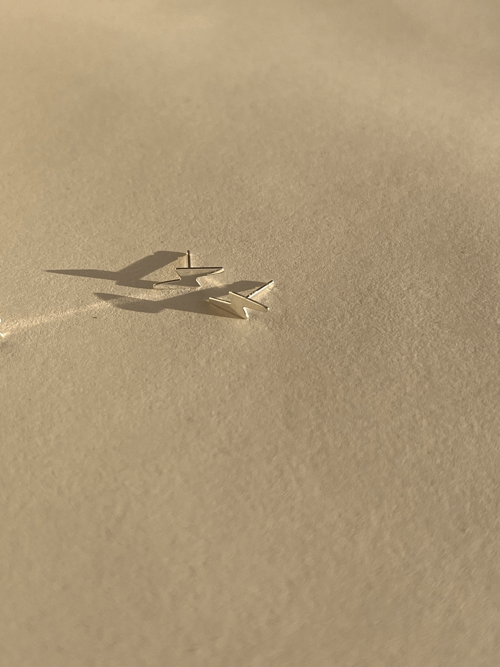 Pair of sterling silver lightning bolt stud earrings shown on a light backdrop
