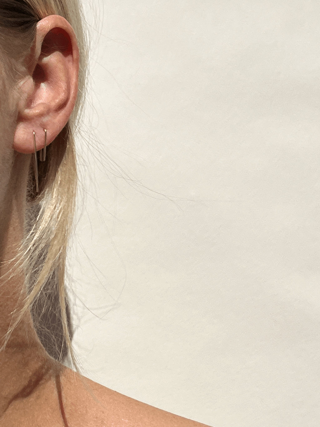 Model wearing long petite staple earrings in yellow gold-filled in her first piercing, with short petite staple earrings in her second piercing, soft focus on ear