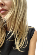 Model wearing the yellow gold-filled minimalist bead chain necklace over a black linen top, necklace styled on top of the shirt