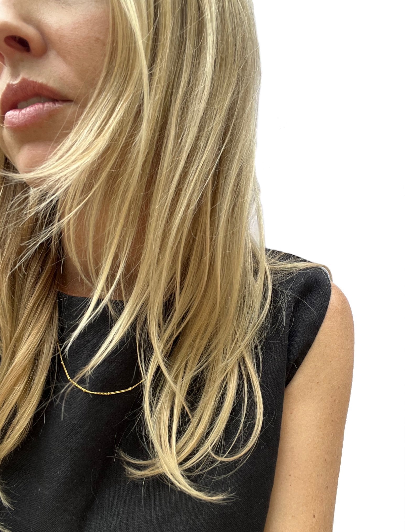 Model wearing the yellow gold-filled minimalist bead chain necklace over a black linen top, necklace styled on top of the shirt