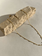 Yellow gold-filled minimalist bead chain necklace draped across a natural rock in warm sunlight