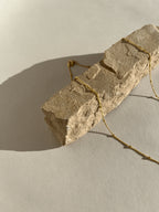 Close-up product shot of the yellow gold-filled minimalist bead chain necklace draped across a rock