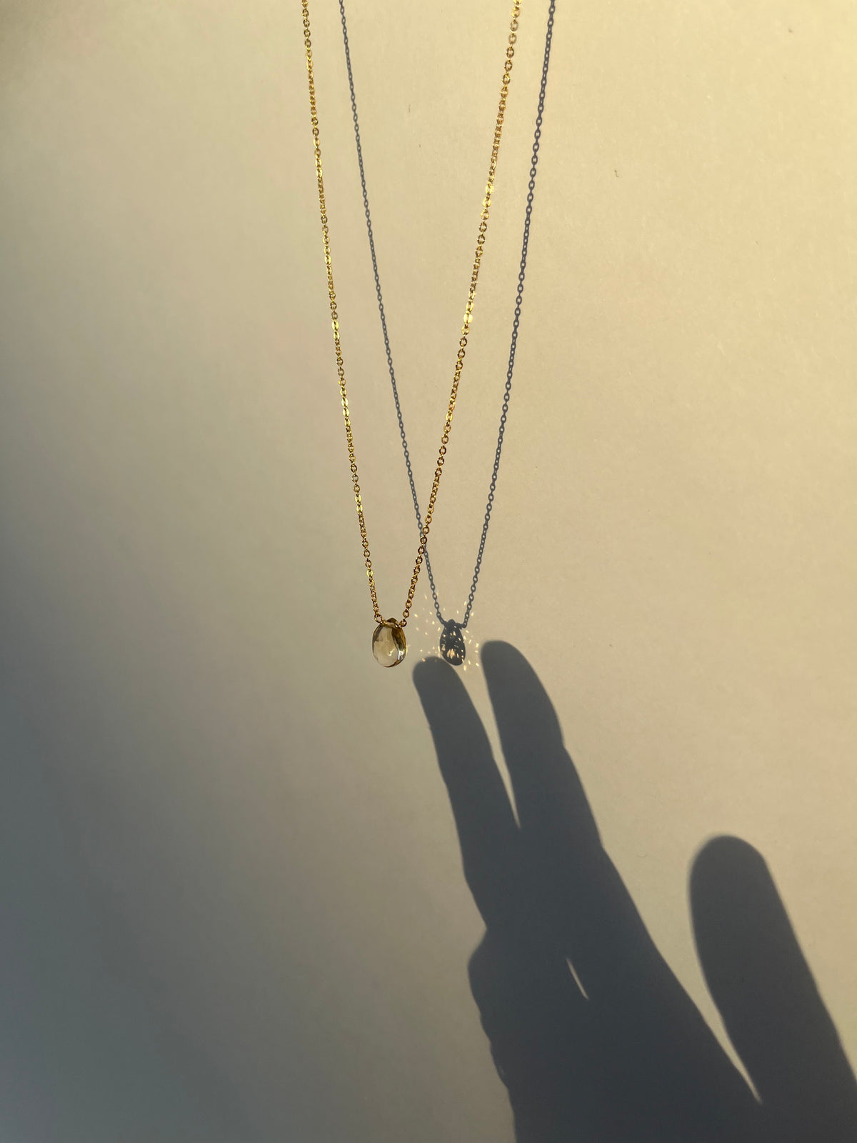 Citrine drop necklace hanging with shadow of hand creating the illusion of a hand touching the necklace drop