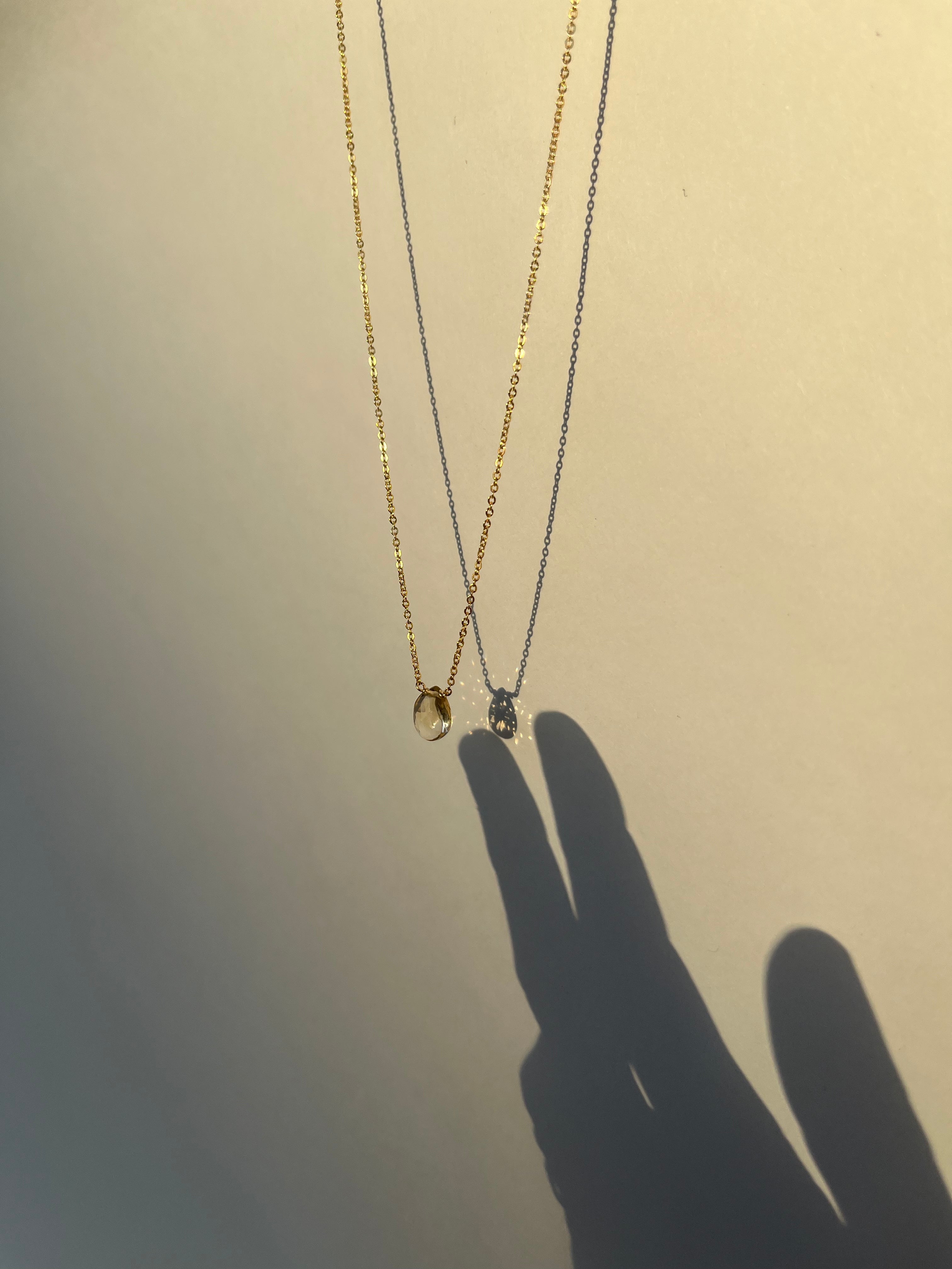 Citrine drop necklace hanging with shadow of hand creating the illusion of a hand touching the necklace drop