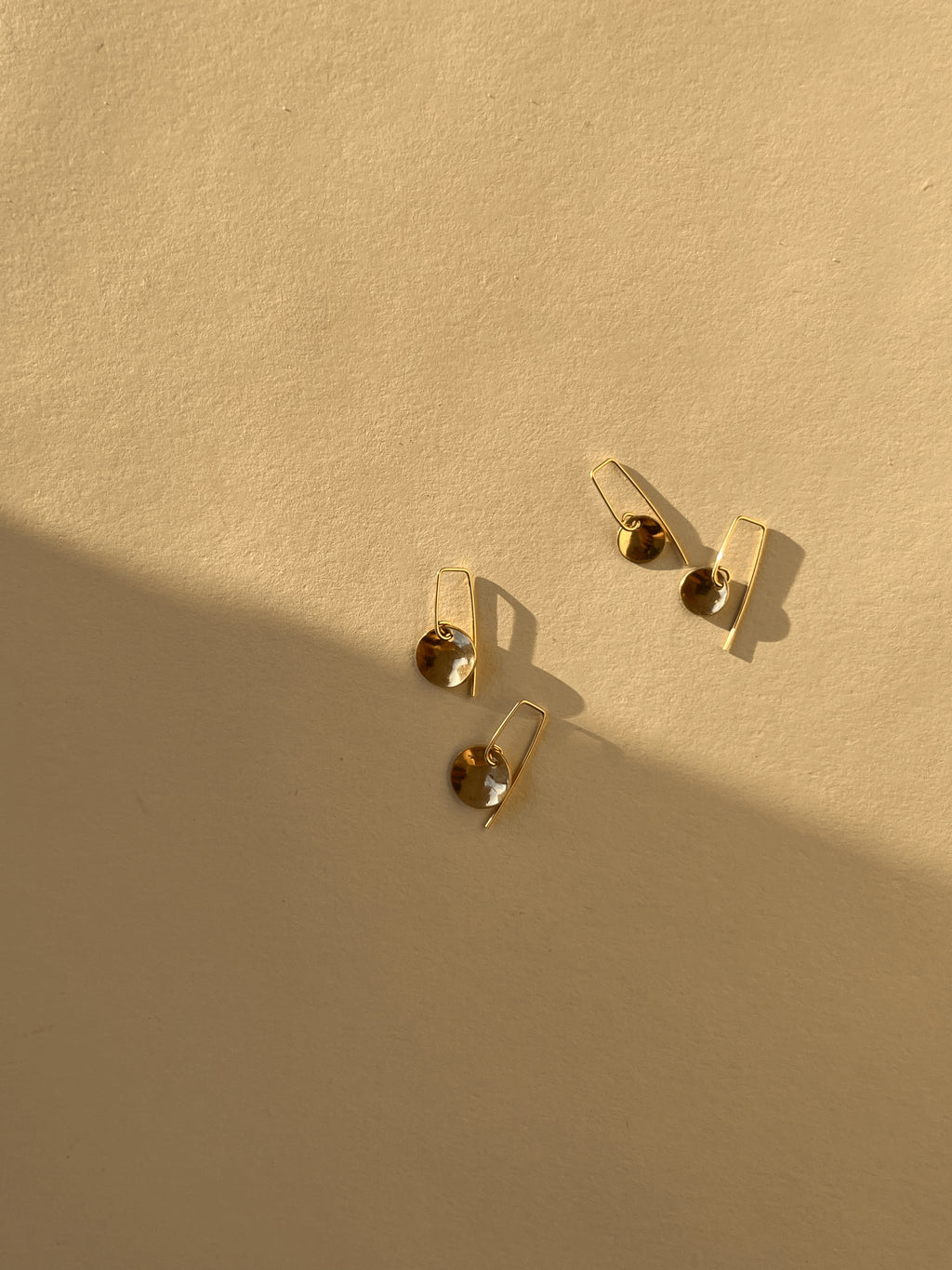 Flat lay of two pairs of Minimalist Disc Dangles in each size disc in yellow gold-filled on neutral background with shadow