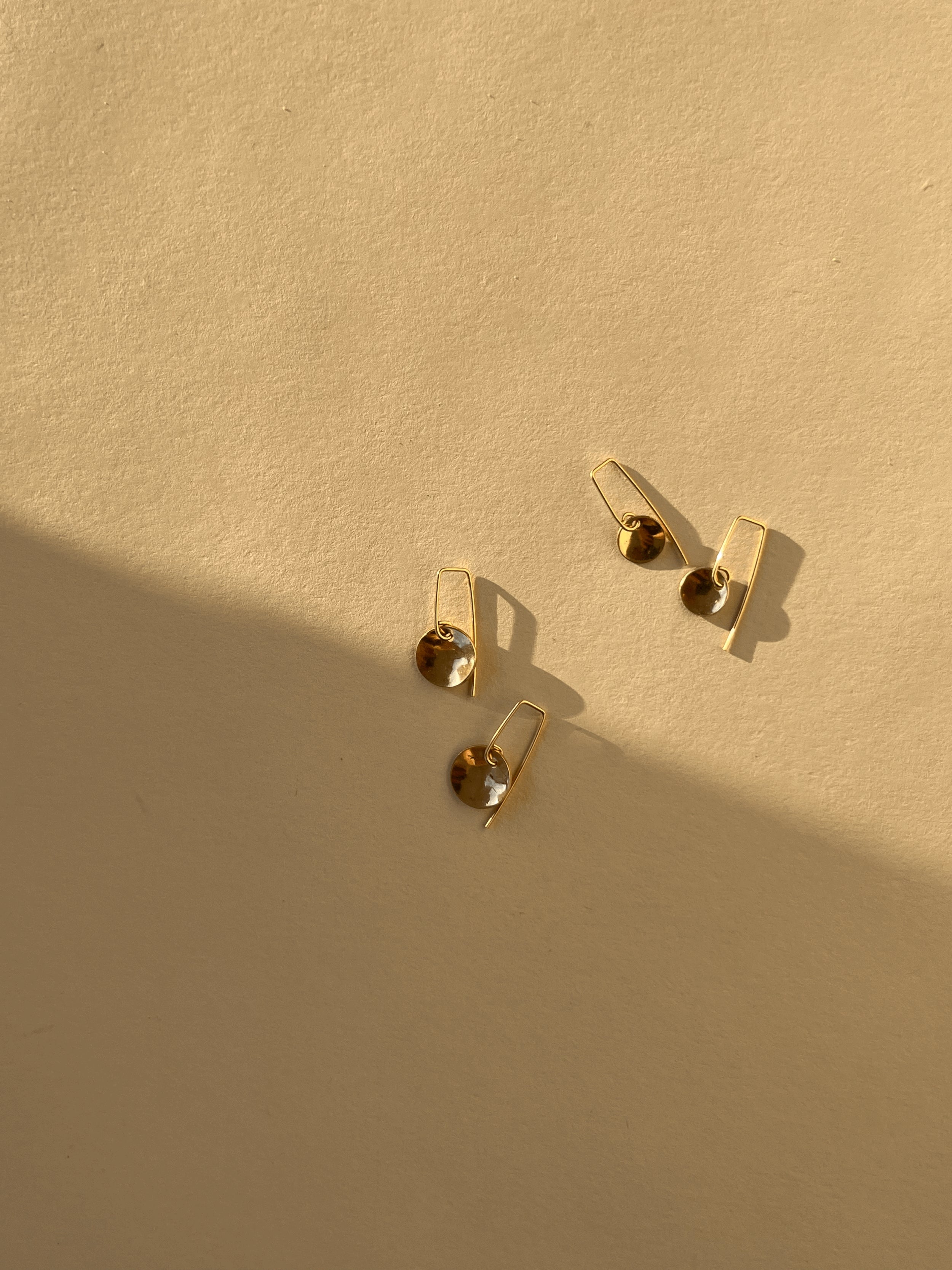 Flat lay of two pairs of Minimalist Disc Dangles in each size disc in yellow gold-filled on neutral background with shadow