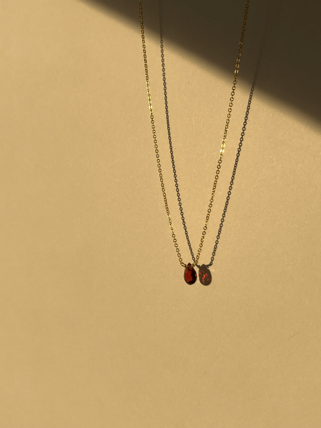 Minimalist yellow gold-filled garnet drop necklace with natural garnet stone pendant suspended against a warm neutral background