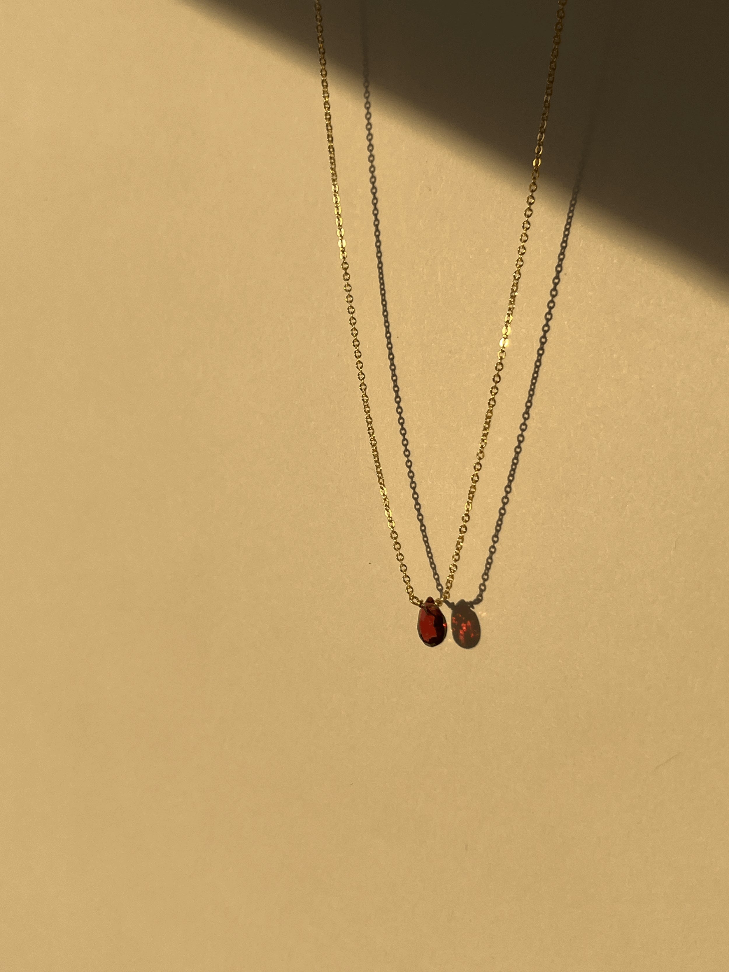 Minimalist yellow gold-filled garnet drop necklace with natural garnet stone pendant suspended against a warm neutral background