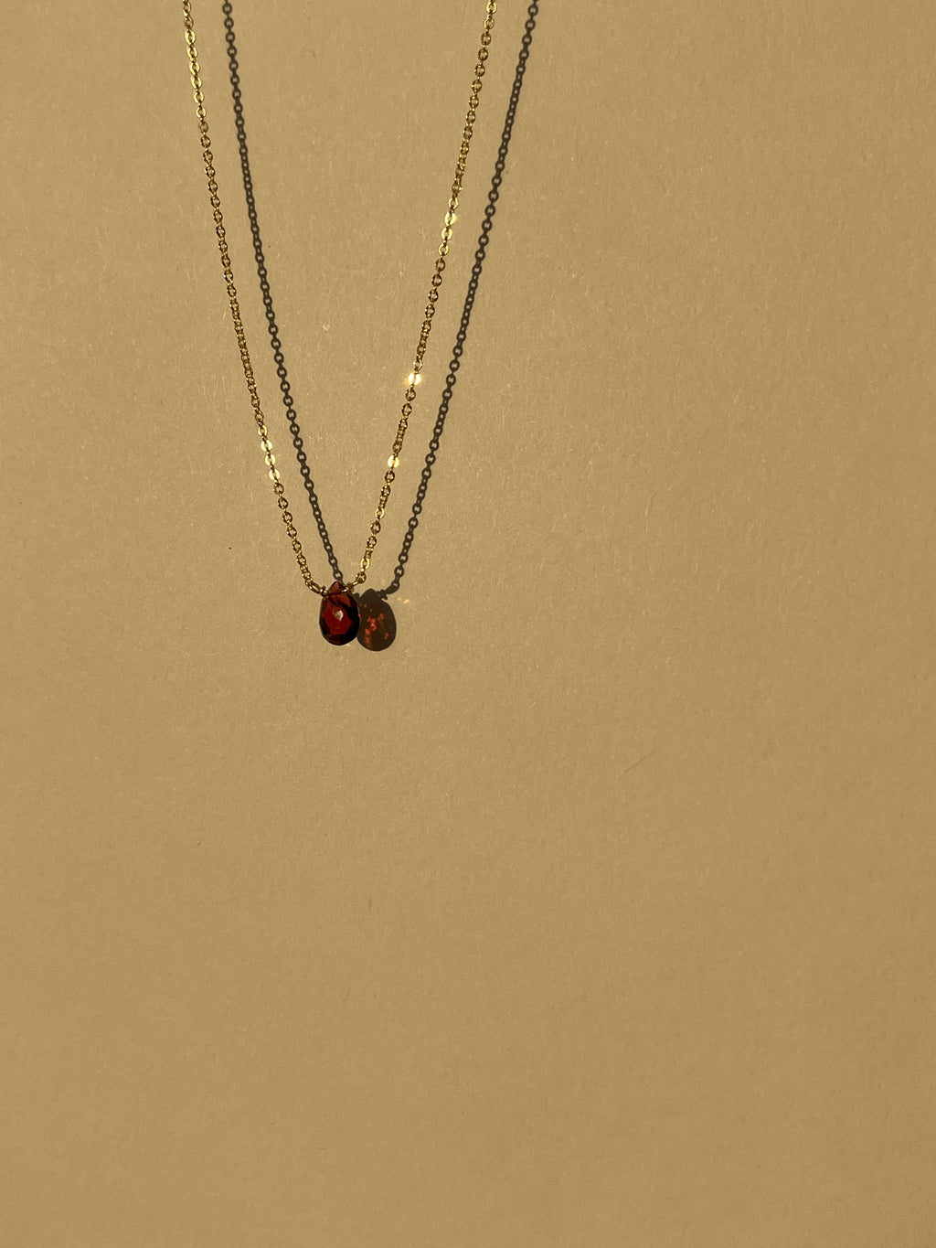 Minimalist yellow gold-filled garnet drop necklace with natural garnet stone pendant suspended against a warm neutral background