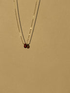 Minimalist yellow gold-filled garnet drop necklace with natural garnet stone pendant suspended against a warm neutral background