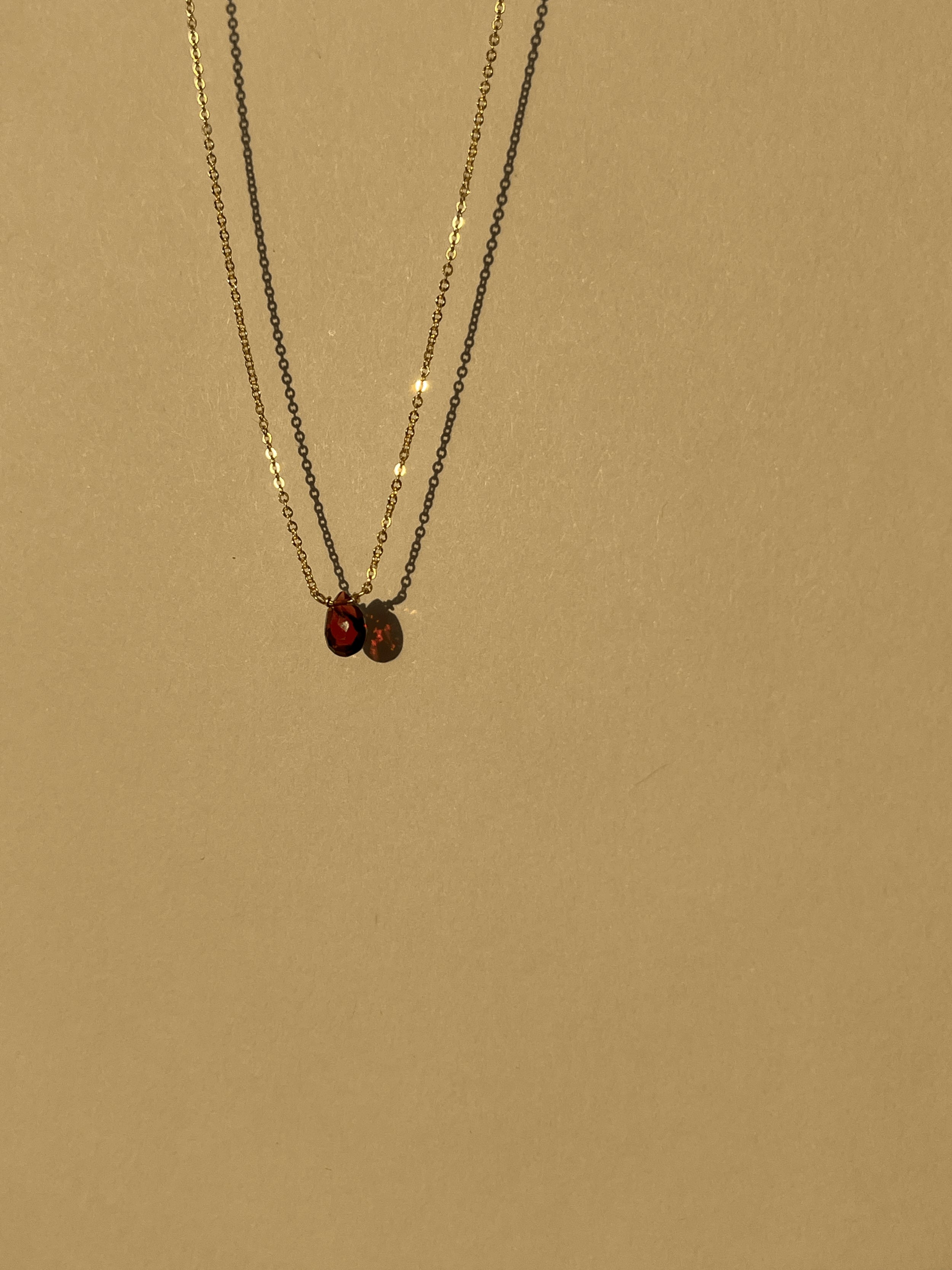Minimalist yellow gold-filled garnet drop necklace with natural garnet stone pendant suspended against a warm neutral background