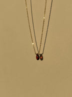 Close-up of minimalist yellow gold-filled garnet drop necklace with natural garnet stone pendant suspended against a warm neutral background