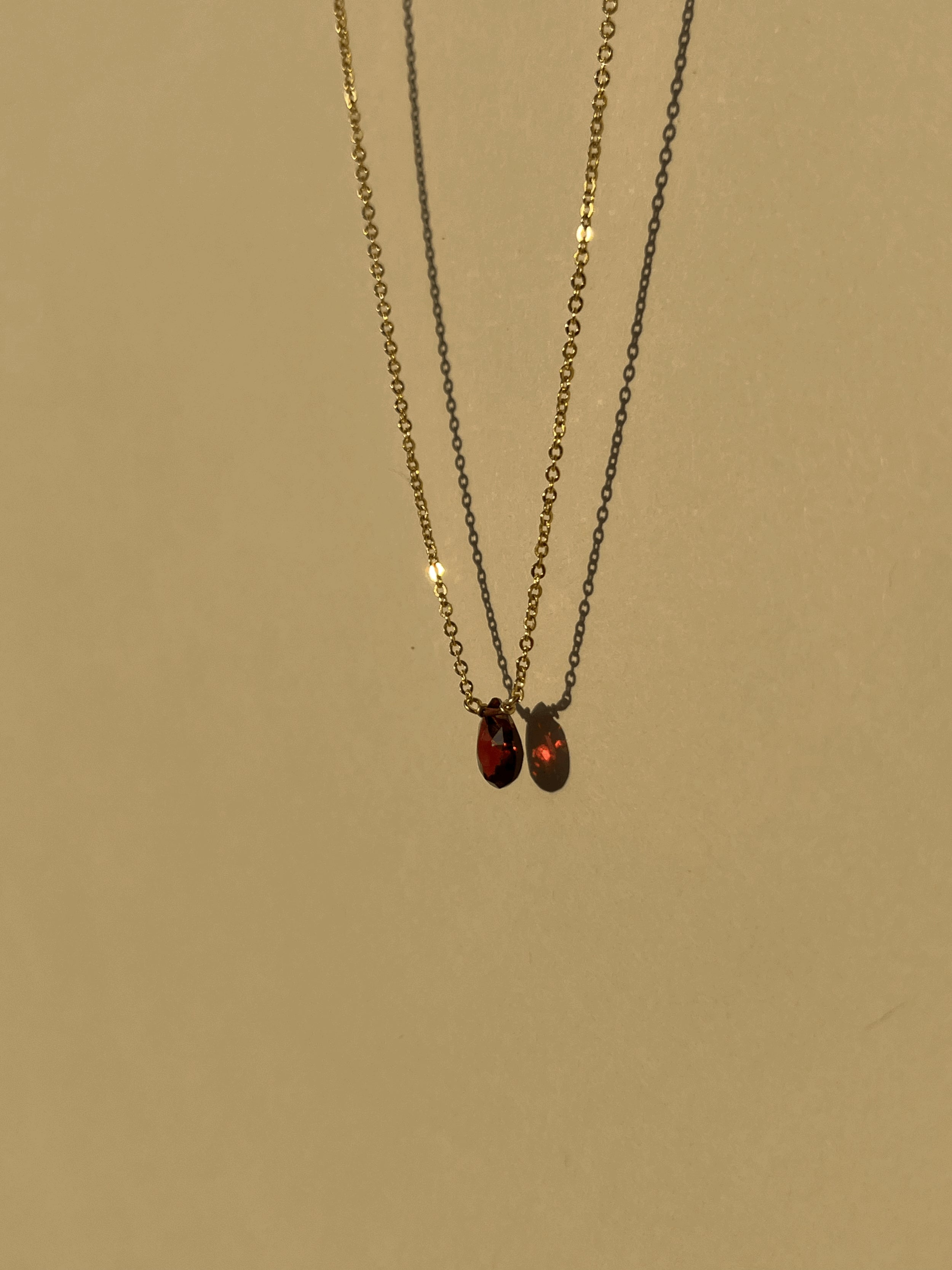 Close-up of minimalist yellow gold-filled garnet drop necklace with natural garnet stone pendant suspended against a warm neutral background