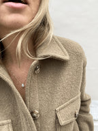 Yellow gold-filled minimalist moonstone drop necklace worn on a model in a beige wool long-sleeve shirt, leaning forward and smiling, showing the centered gemstone