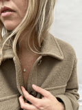 Yellow gold-filled moonstone drop necklace on a model in a beige wool long-sleeve shirt, looking off into the distance, highlighting the delicate chain and natural stone