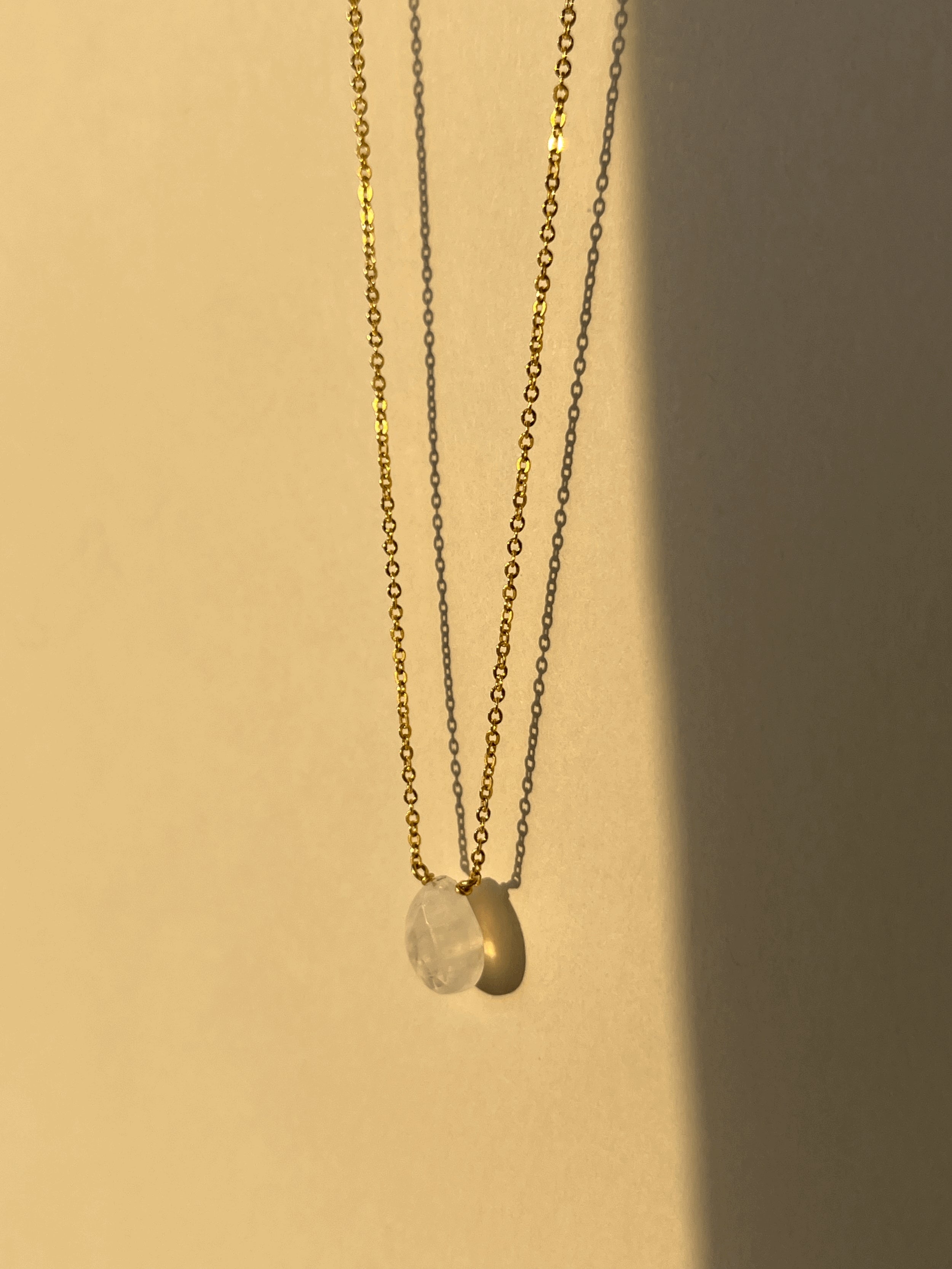 Close-up of yellow gold-filled moonstone drop necklace suspended in warm light, showcasing the semi-translucent natural gemstone and delicate chain