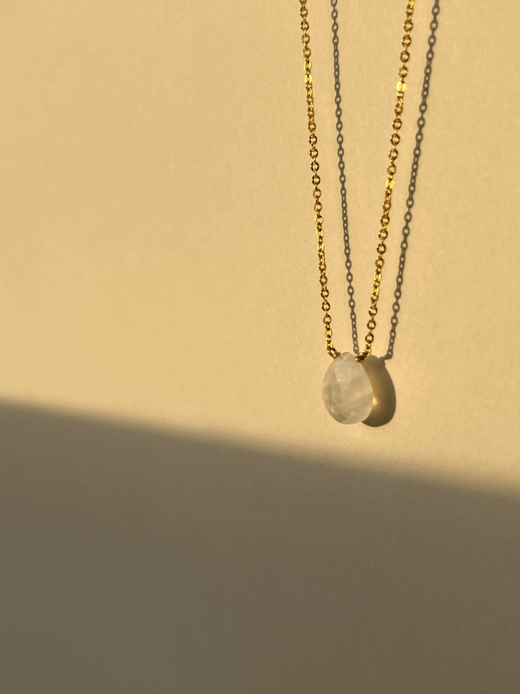 Close-up of yellow gold-filled moonstone drop necklace suspended in warm light, showcasing the semi-translucent natural gemstone and delicate chain