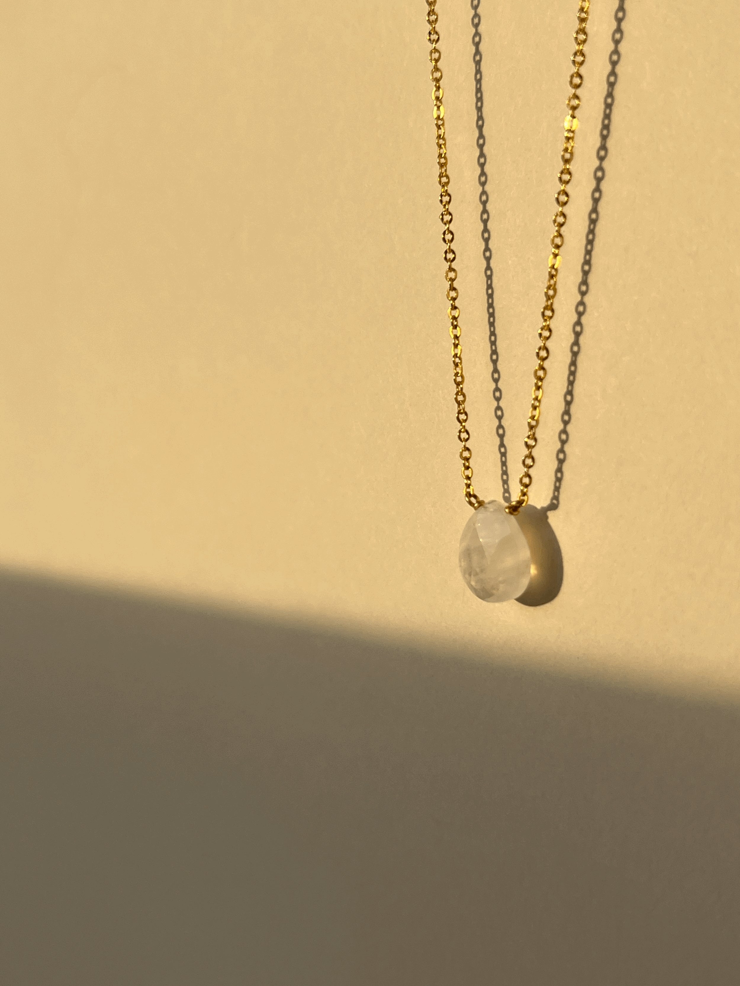 Close-up of yellow gold-filled moonstone drop necklace suspended in warm light, showcasing the semi-translucent natural gemstone and delicate chain