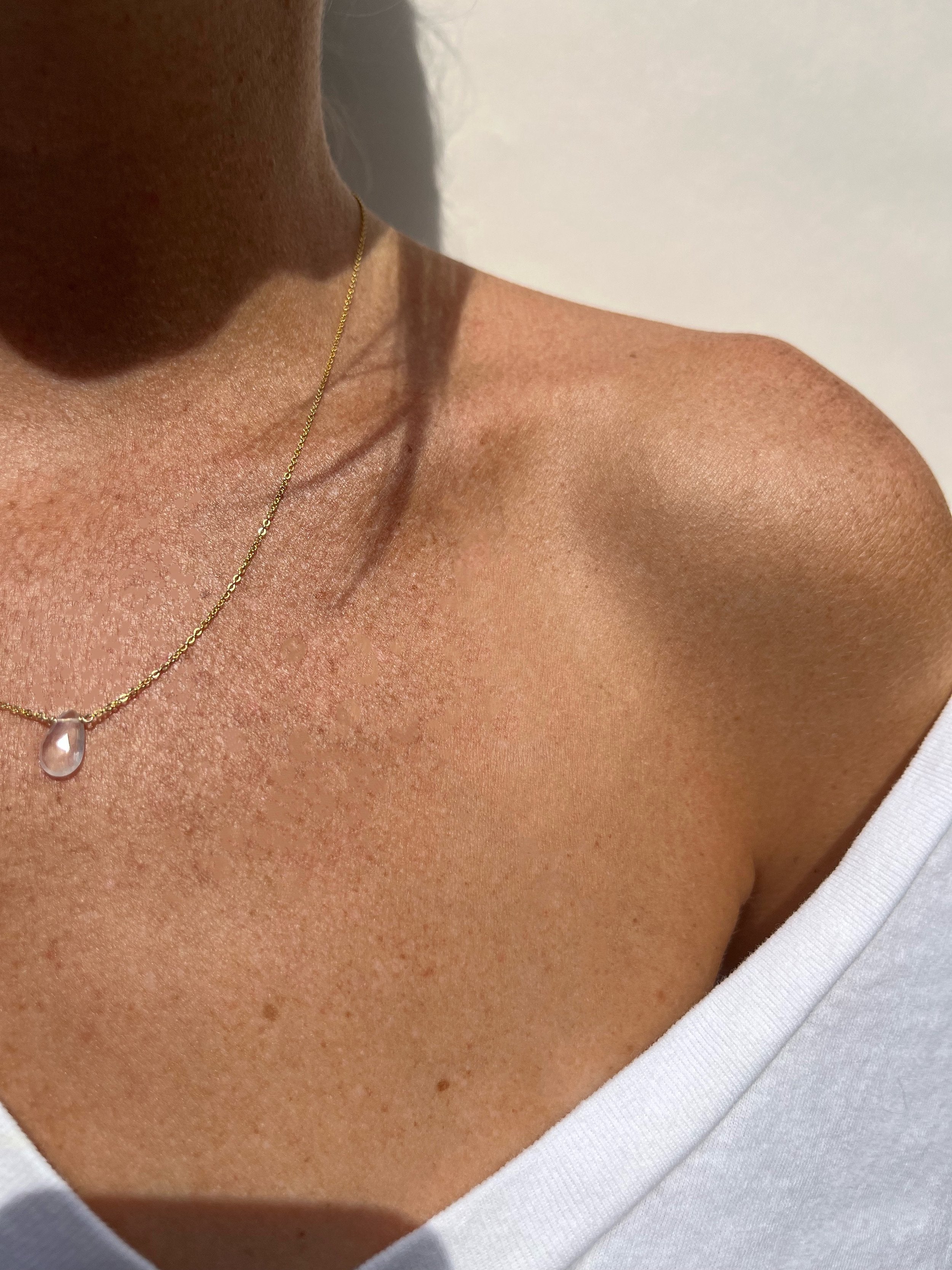 Minimalist Rose Quartz Drop Necklace styled on a model wearing a white V-neck shirt, highlighting the dainty rose quartz drop and gold chain