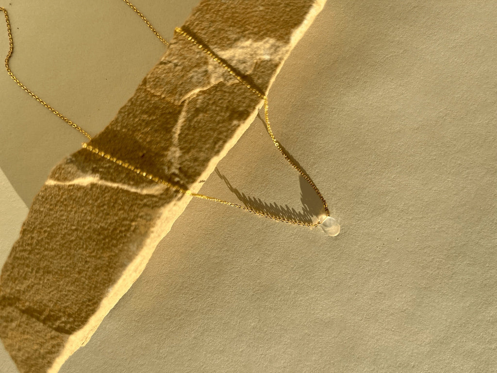 Close-up of the Minimalist Rose Quartz Drop Necklace on natural rock, showcasing the glowing rose quartz drop and the shine of the yellow gold-filled chain