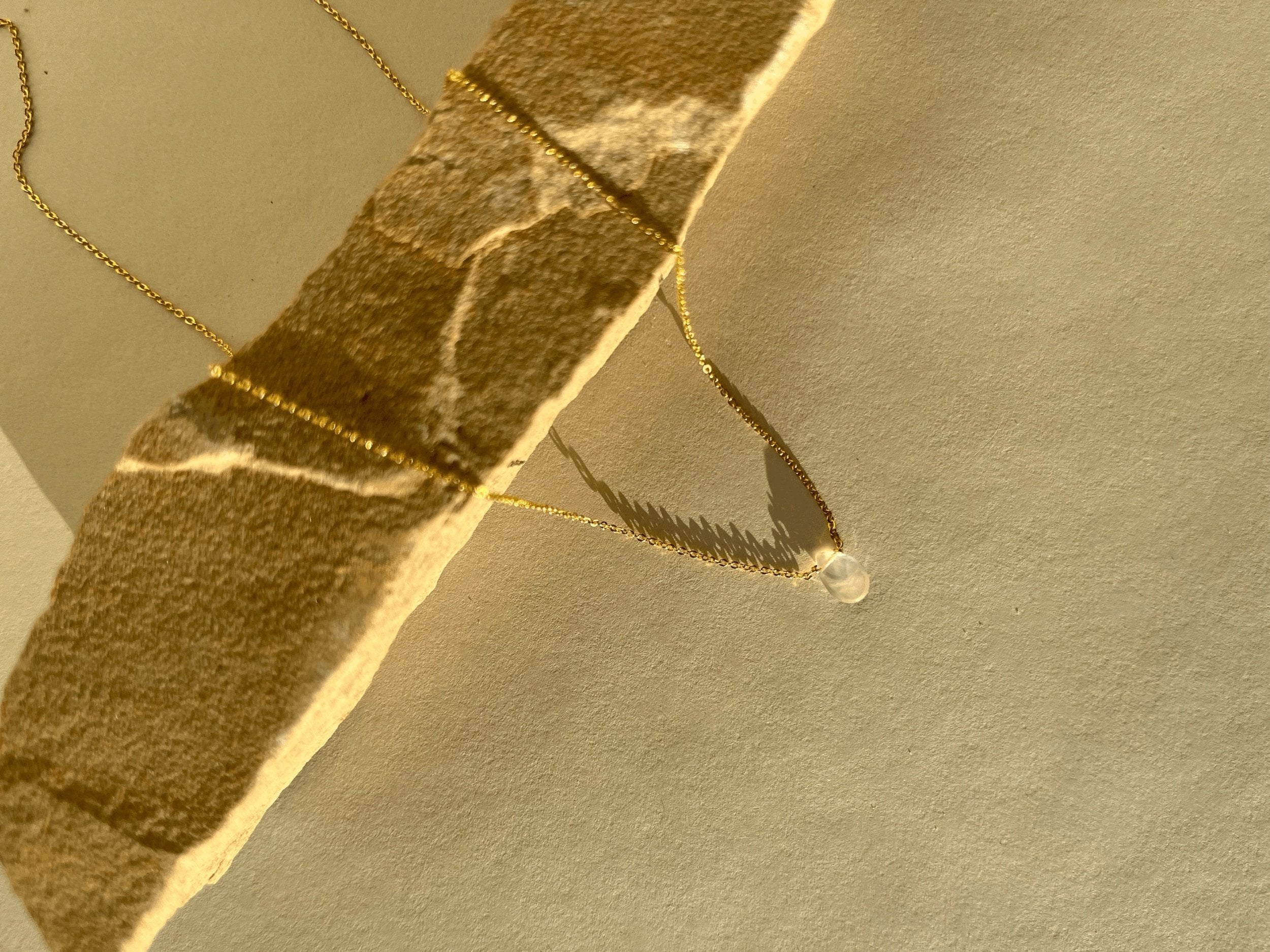 Close-up of the Minimalist Rose Quartz Drop Necklace on natural rock, showcasing the glowing rose quartz drop and the shine of the yellow gold-filled chain