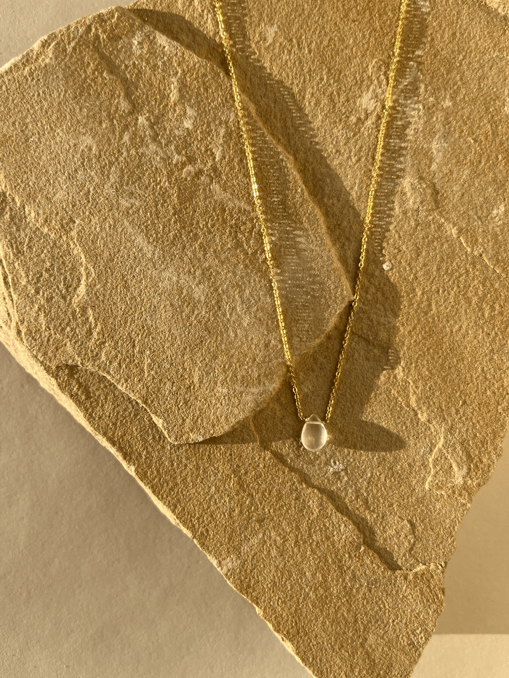 Minimalist Rose Quartz Drop Necklace resting on natural rock, the rose quartz drop glowing and the yellow gold-filled chain catching the light