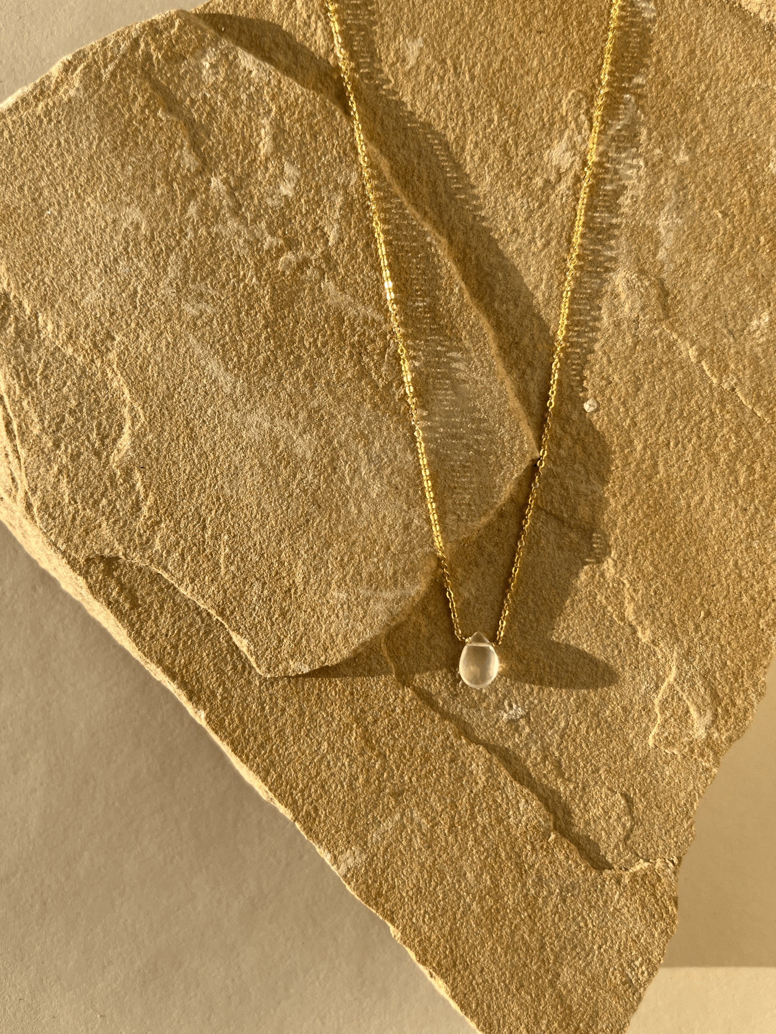 Minimalist Rose Quartz Drop Necklace resting on natural rock, the rose quartz drop glowing and the yellow gold-filled chain catching the light