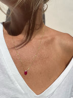 Minimalist ruby drop necklace styled on a model wearing a crisp white v-neck shirt, highlighting the stone’s deep red against a clean, neutral look