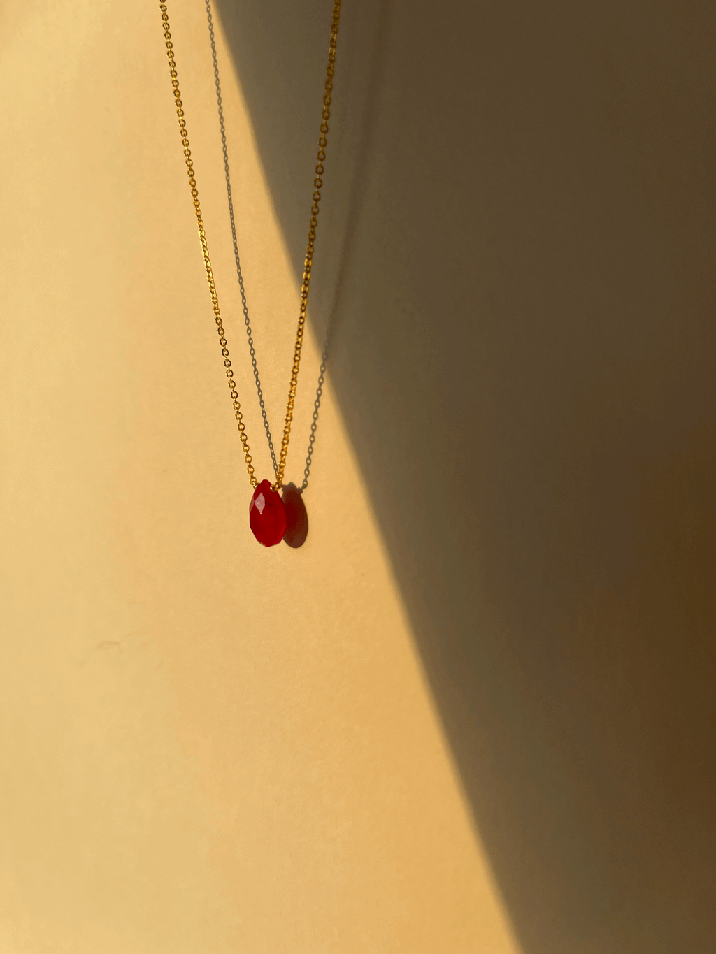 Artistic shot of a minimalist ruby drop necklace floating in soft shadow, suspended against a neutral background for an elegant, modern display
