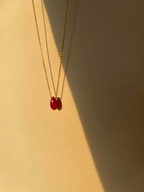 Artistic shot of a minimalist ruby drop necklace floating in soft shadow, suspended against a neutral background for an elegant, modern display