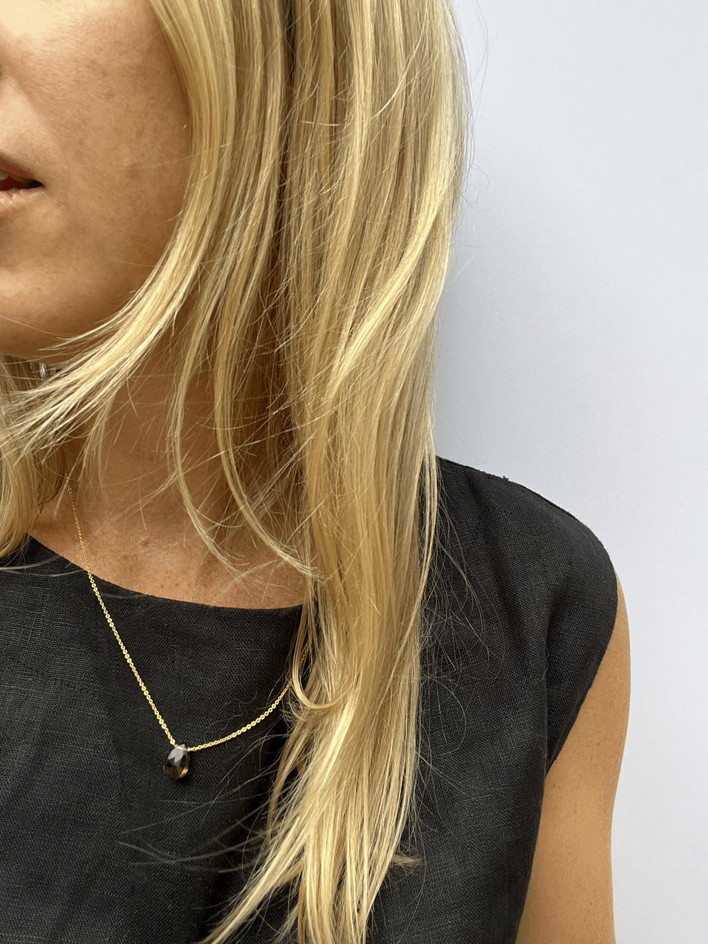 Minimalist smoky quartz drop necklace in yellow gold-filled, worn on a model with a black linen top, showing delicate chain and centered gemstone