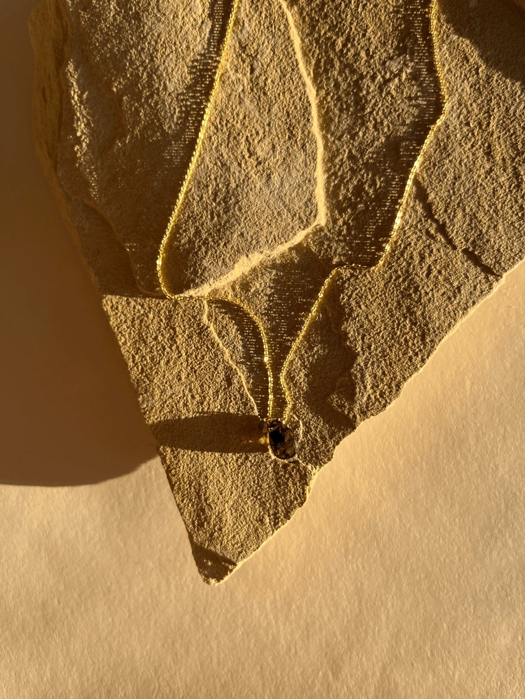 Yellow gold-filled minimalist smoky quartz necklace displayed on a top under warm lighting, highlighting the chain and natural gemstone