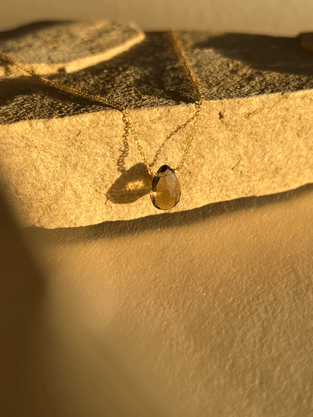 Close-up of yellow gold-filled smoky quartz drop necklace, showing the semi-translucent natural stone and delicate chain under warm light