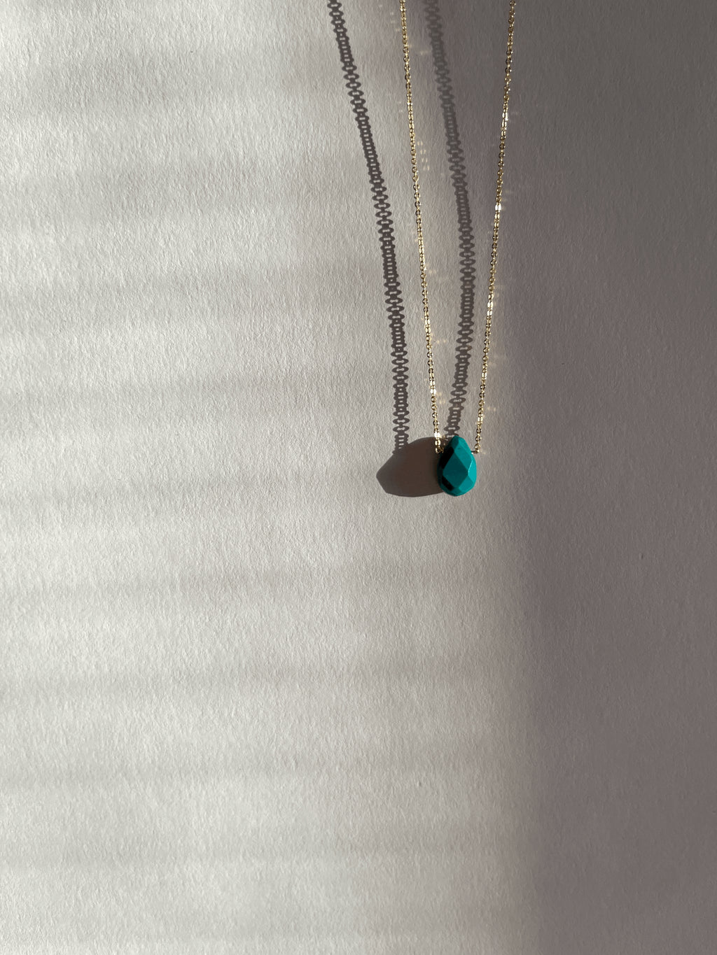 Yellow gold-filled minimalist turquoise necklace photographed at a slight distance, suspended in warm light with soft shadows around the stone