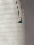 Yellow gold-filled minimalist turquoise necklace photographed at a slight distance, suspended in warm light with soft shadows around the stone