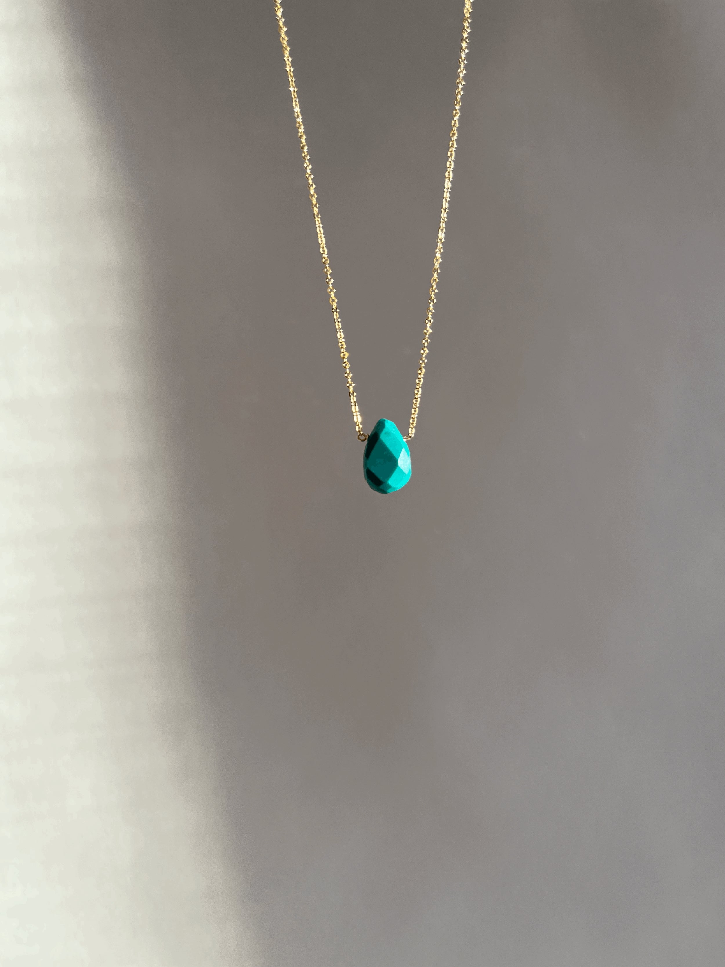 Minimalist turquoise drop necklace in yellow gold-filled, suspended in soft light with natural shadows highlighting the chunky gemstone