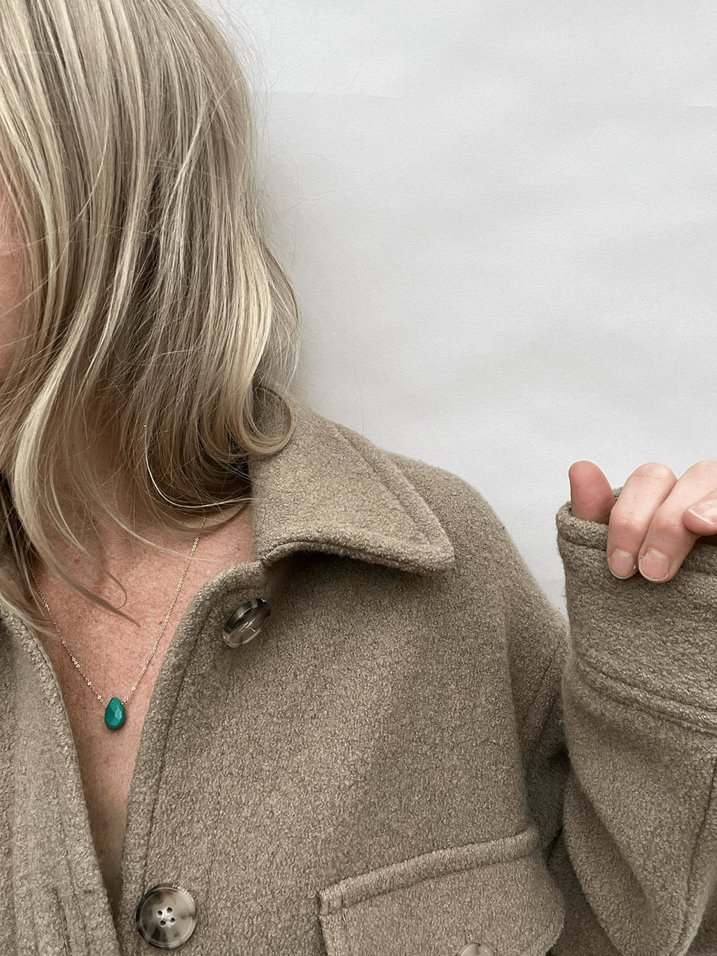 Yellow gold-filled turquoise drop necklace worn on a model in a beige wool long-sleeved shirt, showing the centered gemstone against a neutral look