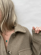 Yellow gold-filled turquoise drop necklace worn on a model in a beige wool long-sleeved shirt, showing the centered gemstone against a neutral look