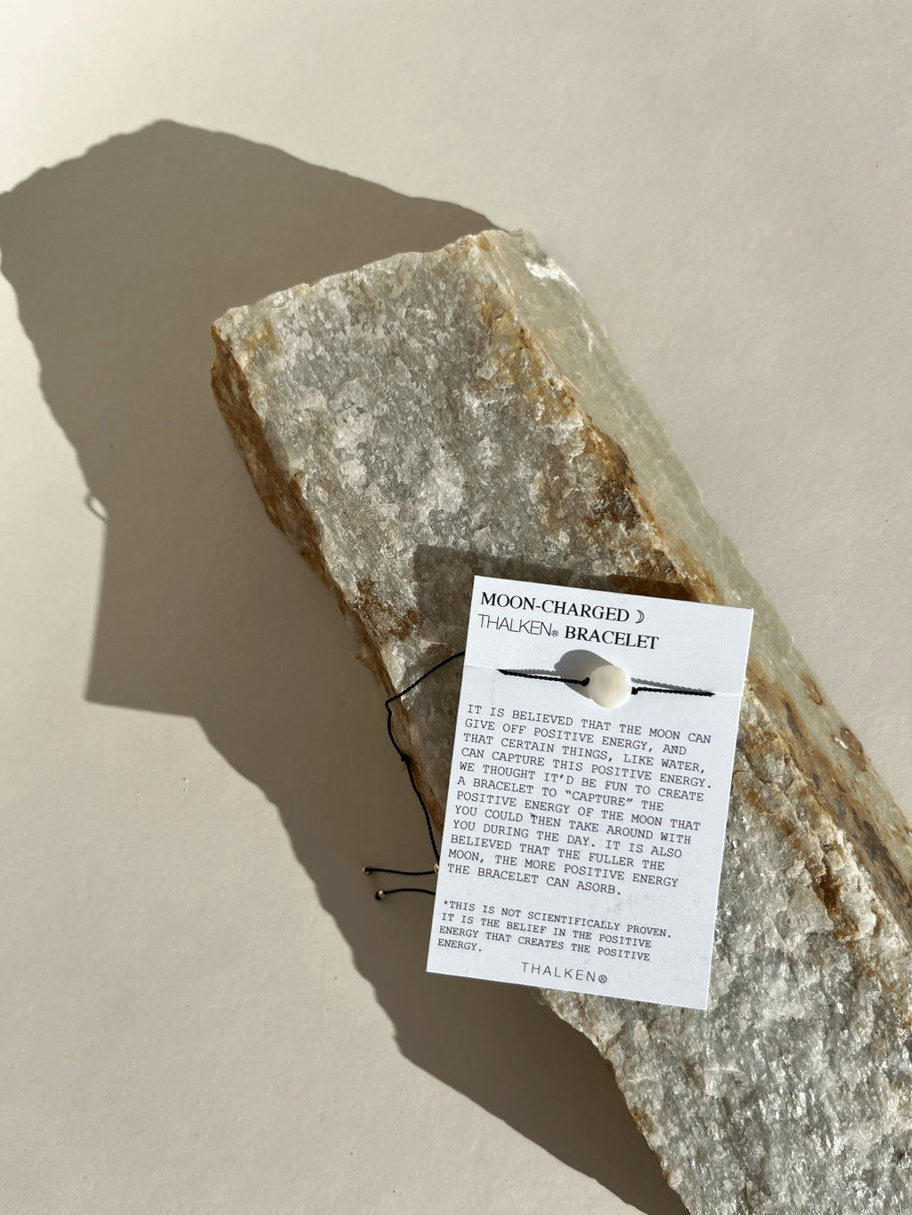 Thalken® Moon Charged bracelet displayed on a mantra card resting on a rock with natural sparkly flecks