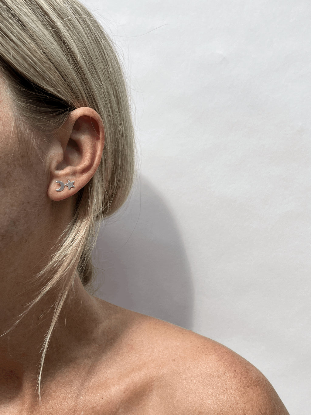 Model wearing a sterling silver moon stud earring in her first ear piercing and a star stud earring in her second ear piercing