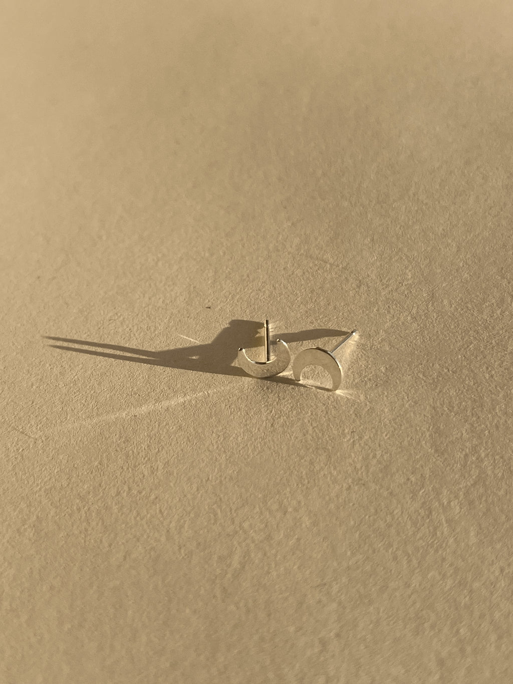 Pair of sterling silver moon stud earrings shown on a light backdrop
