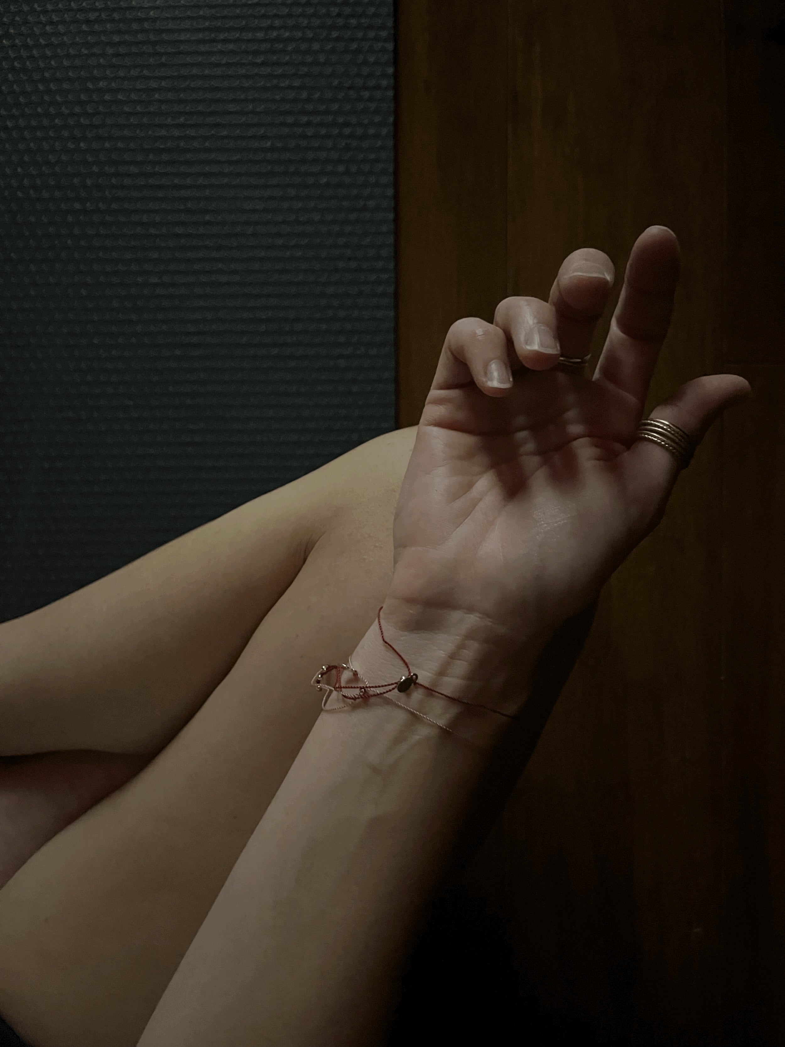 Bird’s-eye view of model sitting cross-legged on a yoga mat, wrists facing up, showing the sliding bead component of the My Energy Is Sacred deep red cord bracelet