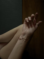 Bird’s-eye view of model sitting cross-legged on a yoga mat, wrists facing up, showing the sliding bead component of the My Energy Is Sacred deep red cord bracelet