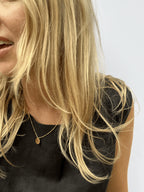 Model wearing the yellow gold-filled My Favorite Necklace with 1mm beads and sliding 10mm disc, smiling and laughing in a black linen top, warm sunlight enhancing the scene