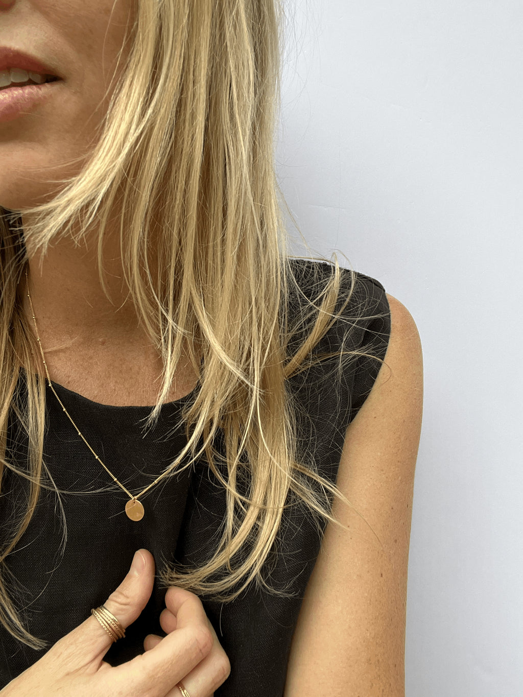 Model wearing the yellow gold-filled My Favorite Necklace with 1mm beads and sliding 10mm disc, styled in a black linen top with warm sunlight highlighting her golden hair