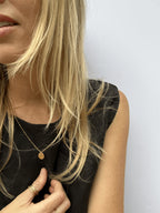 Model wearing the yellow gold-filled My Favorite Necklace with 1mm beads and sliding 10mm disc, styled in a black linen top with warm sunlight highlighting her golden hair